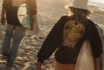Surferzy idący plażą z deskami surfingowymi, ubrani w czarne bluzy.