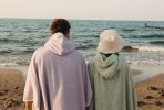 Dwie osoby w płaszczach na plaży, patrzą na morze.