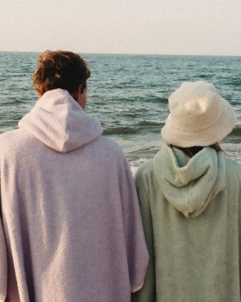 Dwie osoby w płaszczach na plaży, patrzą na morze.
