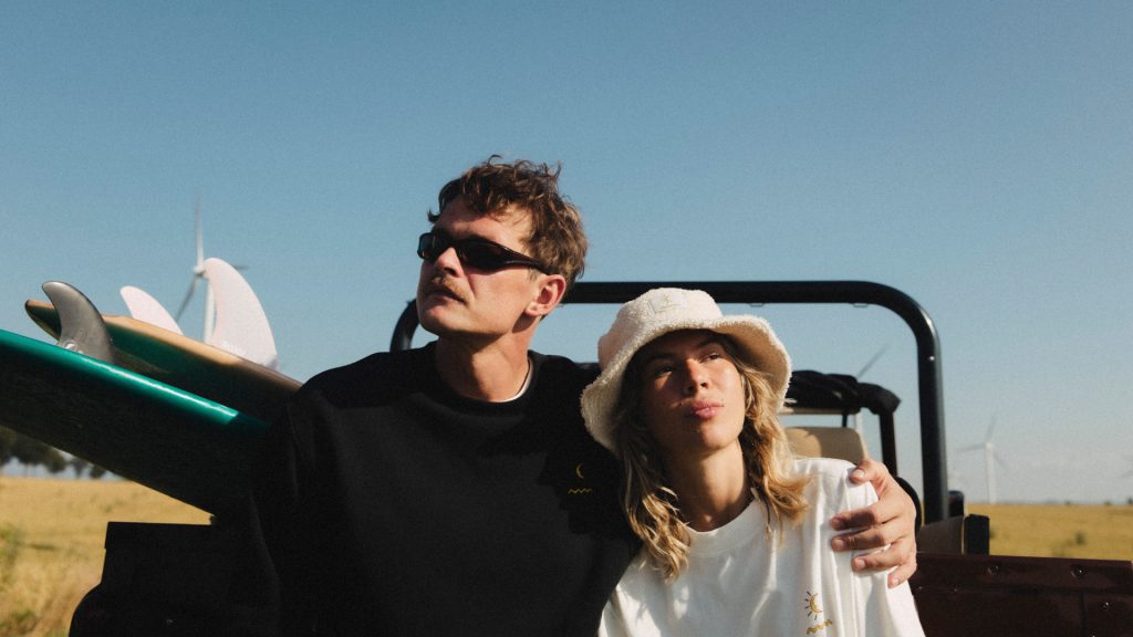 Para z deskami surfingowymi na tle wiatrowych turbin.