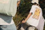 Dwie osoby w letnich ubraniach idą przez zarośla, jedna ma koszulkę z nadrukiem.