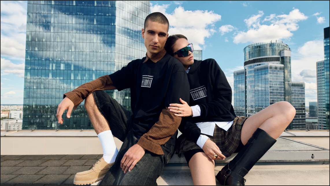 Para przytulająca sie, mają na sobie czarne koszulki z krótkim rekawem ze wzorem maszyny Paczkomat i napisem "Support Your Local Paczkomat"