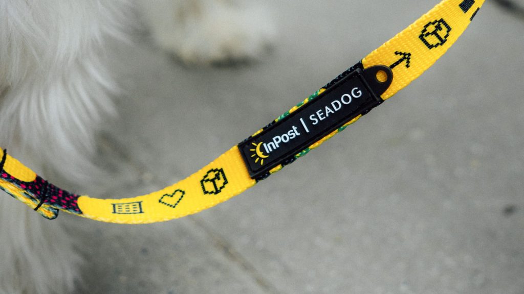 Zbliżenie na smycz ze współpracy InPost i SeaDog. Napis "Smycz w jedną, paczka w drugą" oraz gumowa metka z logo.