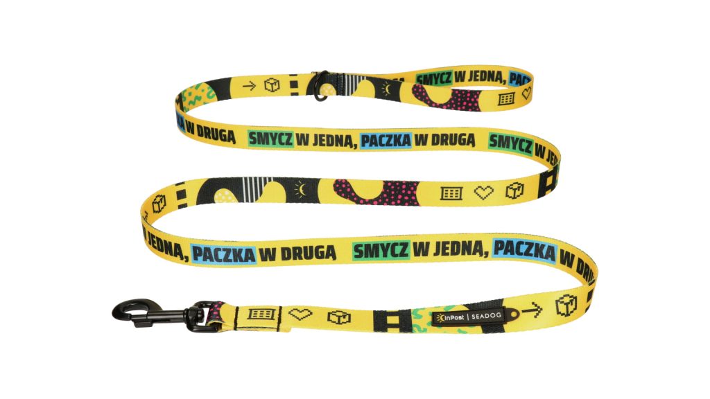 Żółta smycz z napisem "SMYCZ W JEDNA, PACZKA W DRUGA" oraz różnymi symbolami.